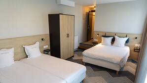 Quarto de hotel com duas camas, um guarda-roupa, um espelho e piso estampado.