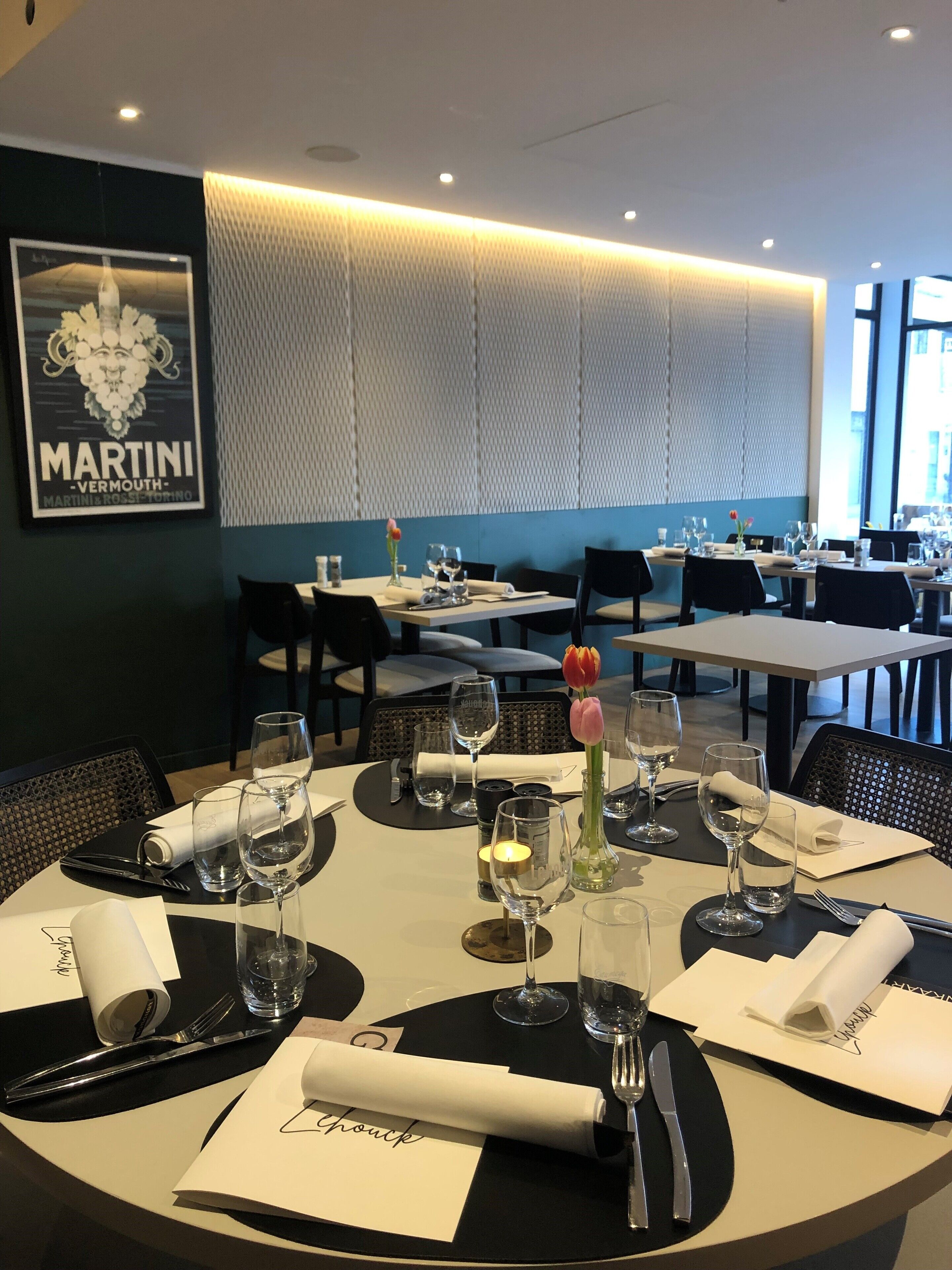A restaurant interior with tables set for dining, a Martini poster on the wall, and a view of the dining area.