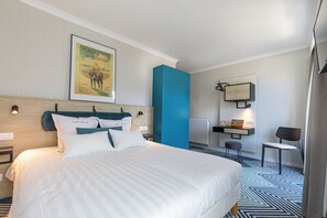 Habitación de hotel con una cama grande, un escritorio con silla, un radiador y un cuadro enmarcado en la pared.