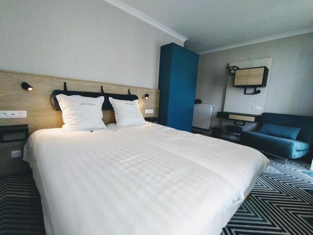 Quarto de hotel com uma cama grande, uma parede de destaque azul, uma escrivaninha e uma cadeira.