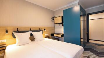 A hotel room with a large bed, a nightstand, a desk, and a wardrobe.