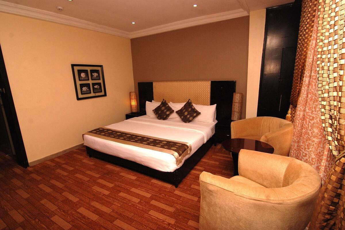 A hotel room with a large bed, a chair, a wall-mounted picture, and a patterned curtain.