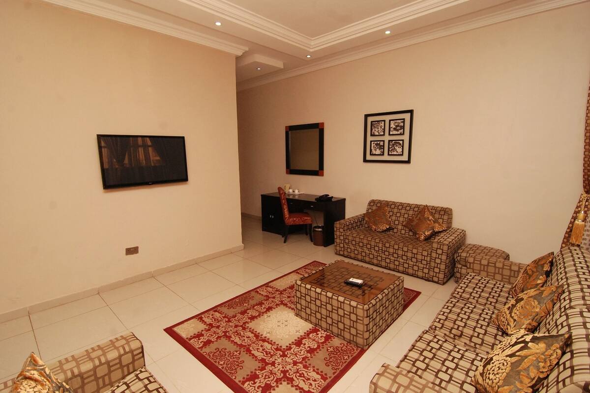 A living room with patterned sofas, a coffee table, a TV, and a desk with a chair.