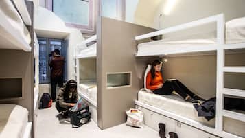 Un dormitorio con literas, una ventana y una persona usando una computadora portátil.