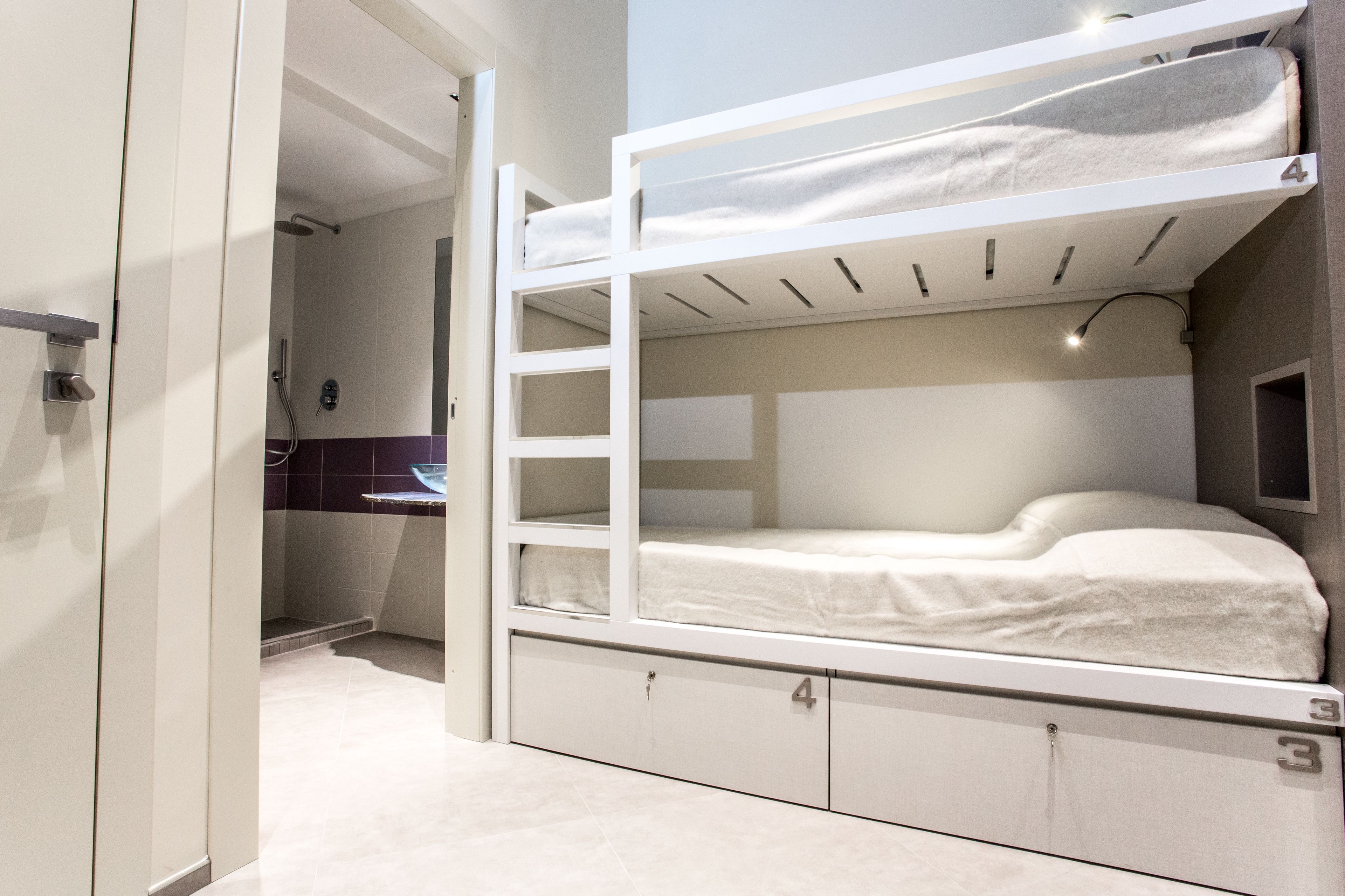 Un lit superposé avec un bureau et une étagère dans une pièce dont le sol est carrelé et qui possède une porte donnant sur une autre pièce.