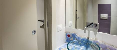 A bathroom with a glass sink, a mirror, and a door leading to another room.
