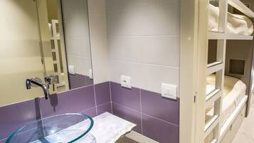 Une salle de bain avec un lavabo en verre, des carreaux violets et blancs, un miroir et un lit superposé avec du linge de lit blanc.