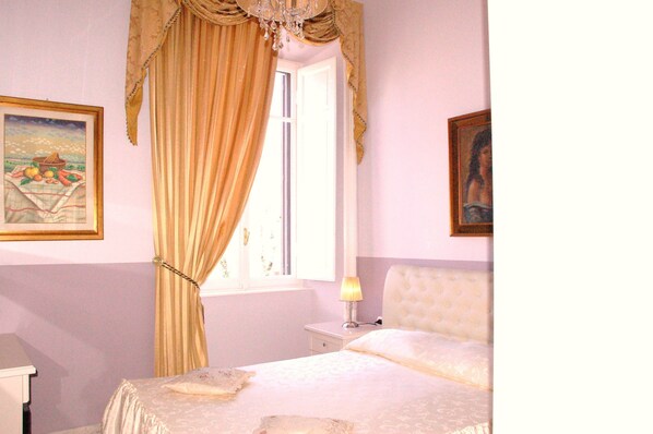 Une chambre à coucher comprenant un lit, une table de chevet, une lampe, une fenêtre avec des rideaux et deux tableaux encadrés accrochés aux murs.