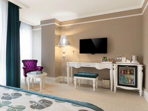 A hotel room with a bed, a purple armchair, a small table, a desk, a television, and a minibar. - Metropolitan Hotels Taksim (Istanbul)