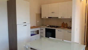 A compact kitchen with white cabinets, a glass table, and a built-in dishwasher.