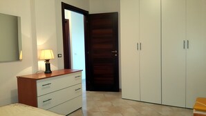 Un dormitorio con una cama, un tocador, una lámpara, un armario y una puerta.