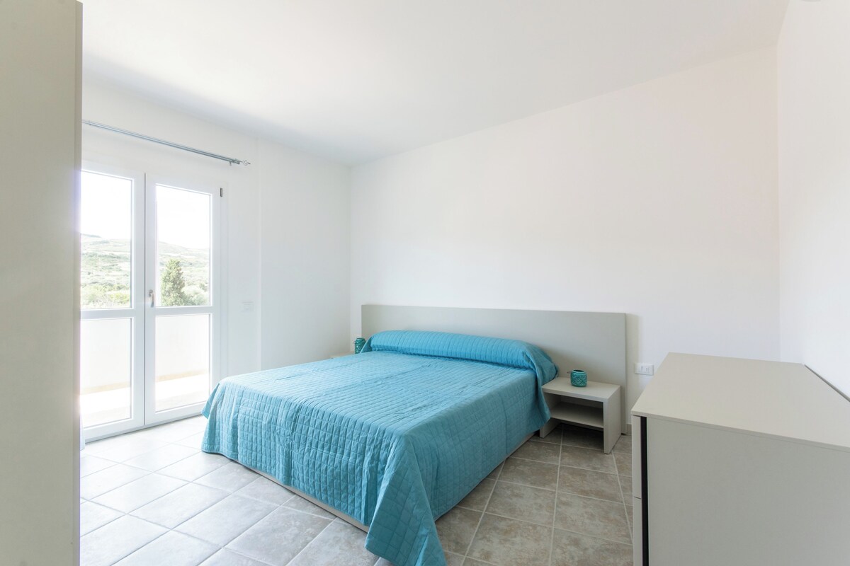 A bedroom with a bed, a nightstand, a bench, and a white cabinet.