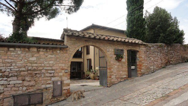 A stone building with a tiled roof, an arched entrance, and a small dog in front. - La Terrazza di spello (Spello)