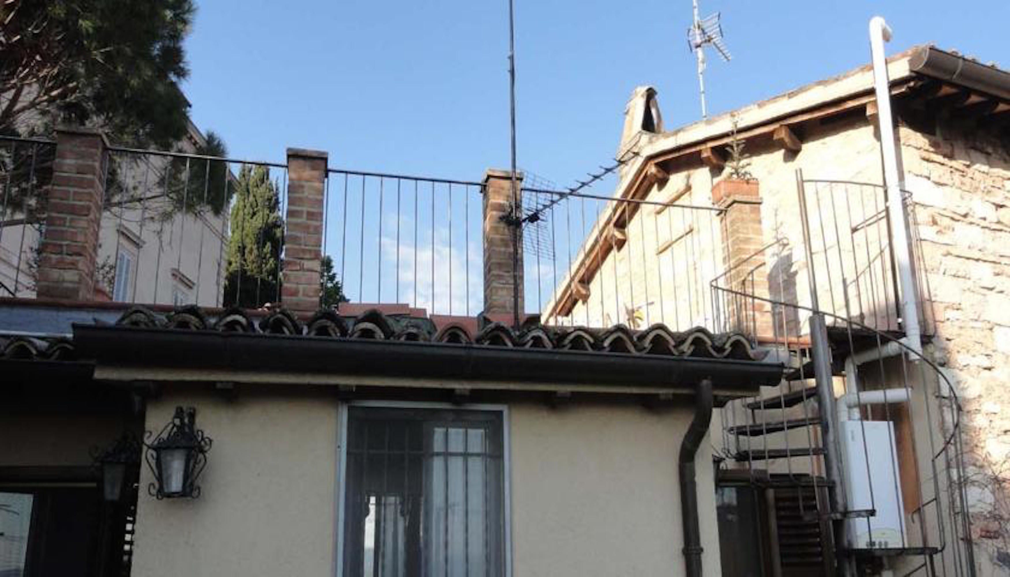 A building with a tiled roof, a chimney, and a metal fence.