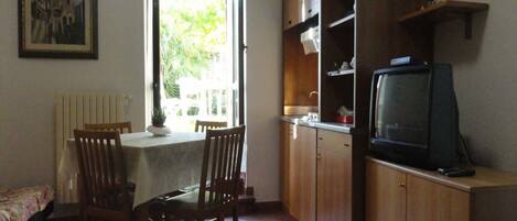 A compact living space with a dining area, a kitchen with wooden cabinets, and a television.