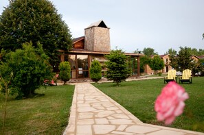A stone pathway leading to a building with a stone chimney and wooden exterior. There are green bushes and a pink flower in the foreground. - Agva Gizemli Nehir Hotel (Sile)