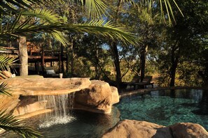 A pool with clear water, surrounded by rocks and palm trees.