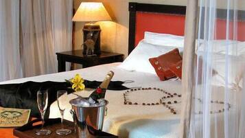 A hotel room with a bed, a nightstand with a lamp, a bottle of champagne, and a flower.