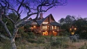 A large, two-story house with a balcony, surrounded by trees and a grassy area. - Lukimbi Safari Lodge (Nkomazi)