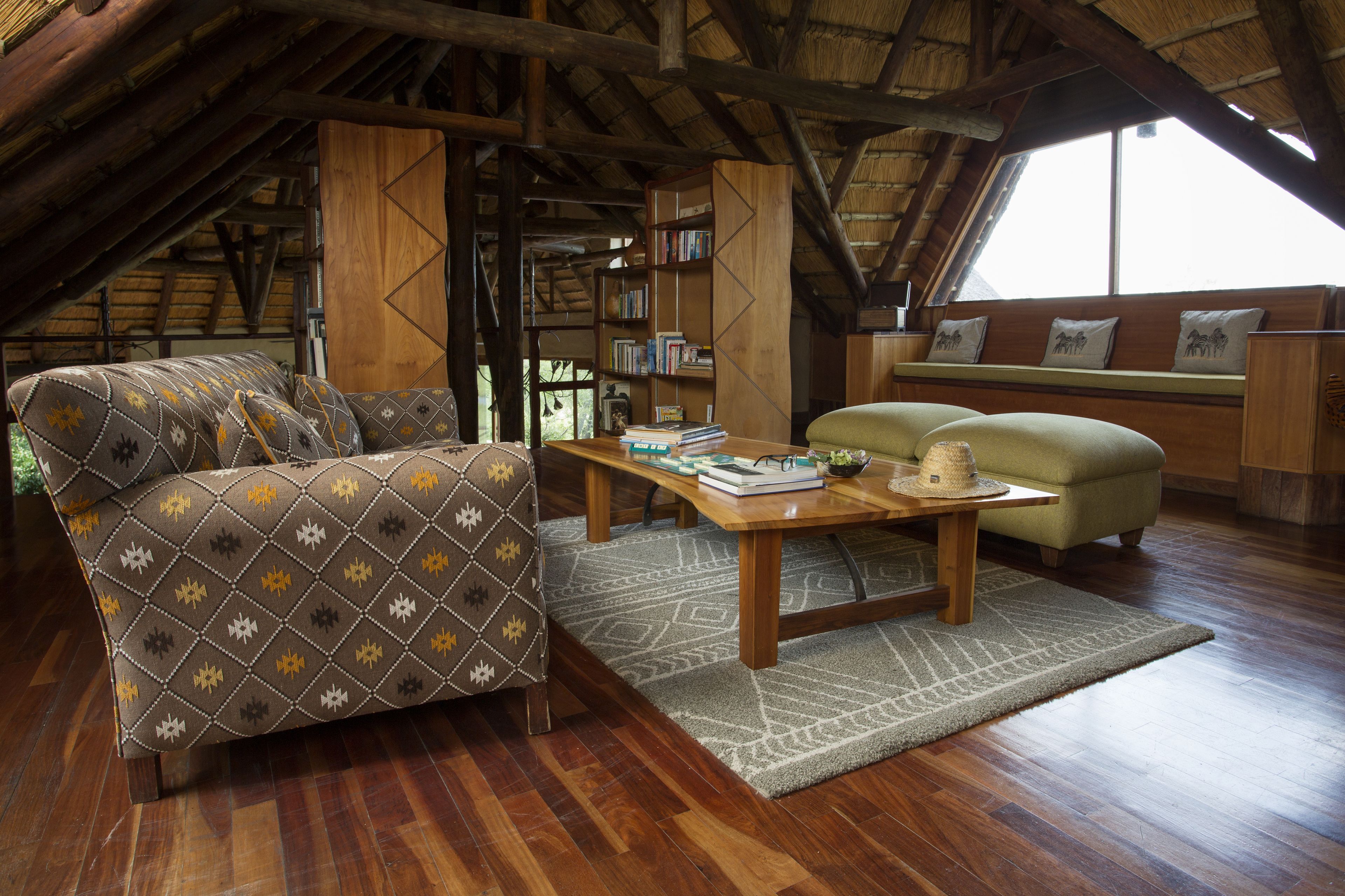 Een zolderkamer met een houten plafond, een bank, een klein tafeltje en een boekenkast.
