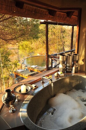 Uma área de spa com uma grande banheira de hidromassagem, um deck de madeira e vista para uma paisagem natural.