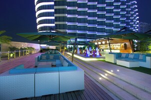 Un hotel moderno con bar en la azotea, mesas al aire libre y vistas a un edificio de gran altura.