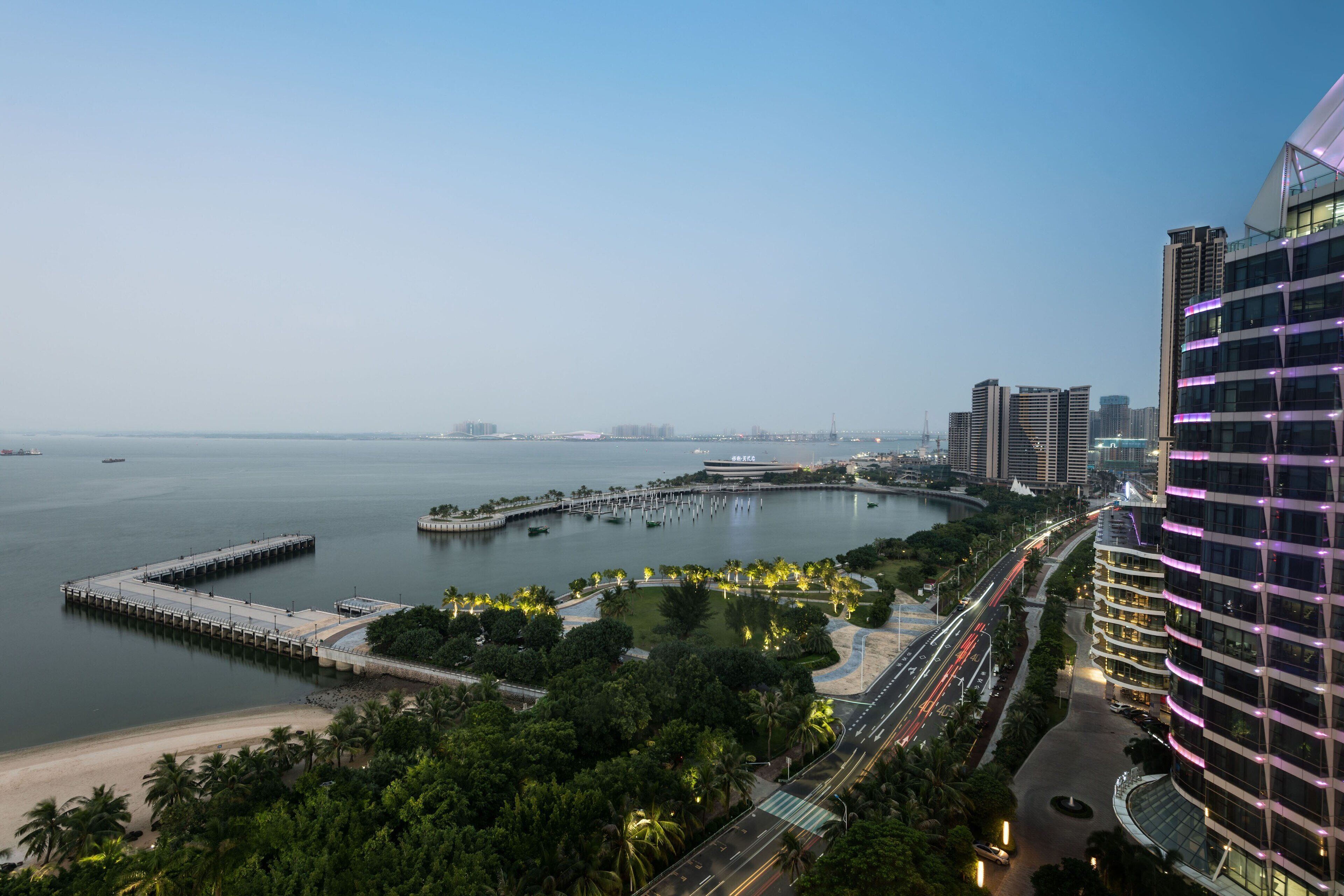 A waterfront urban area with modern buildings, a marina, and a curved road with traffic lights.