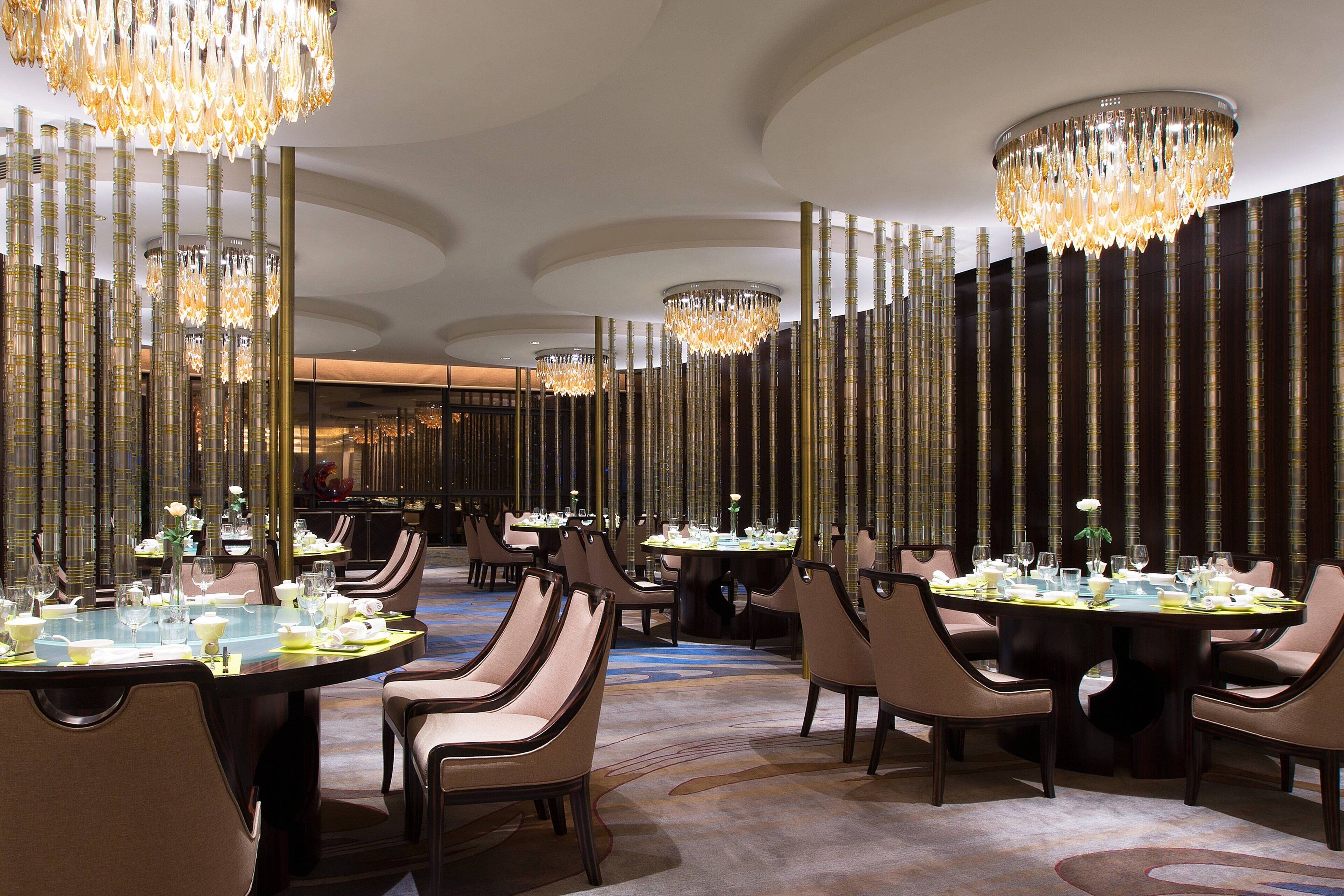 A formal dining area with multiple tables set for service, elegant chandeliers, and a sophisticated interior design.