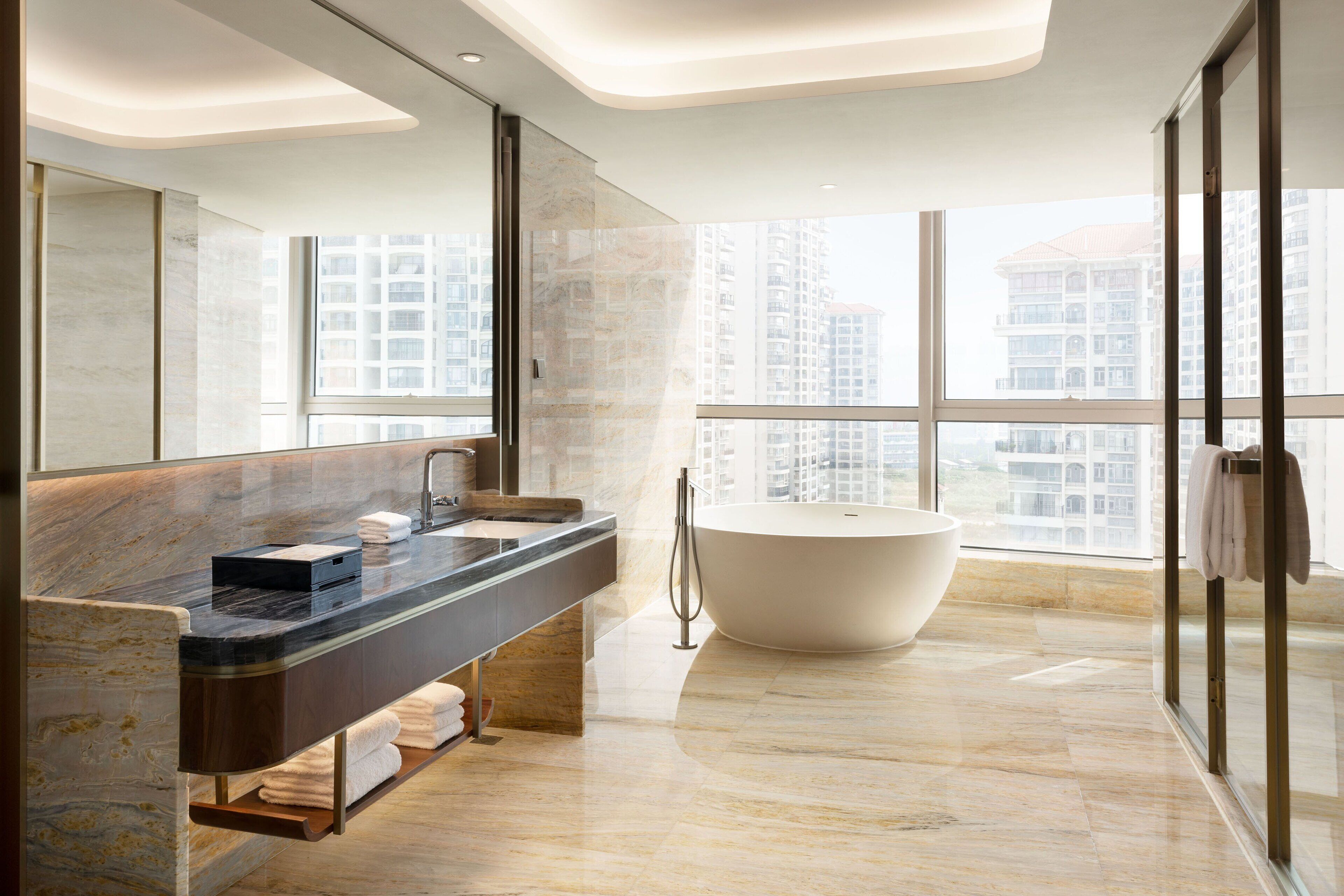 A modern bathroom with a large bathtub, a long vanity with a marble countertop, and a large mirror.