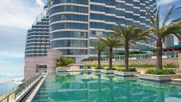 Un hotel moderno dal design curvo, con piscina sul tetto e palme.