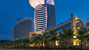Un hotel moderno con una caratteristica torre di osservazione circolare, diversi edifici alti e palme sullo sfondo.
