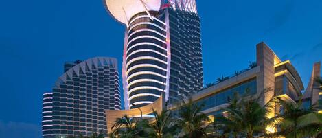 A modern hotel with a distinctive circular observation tower, multiple high-rise buildings, and palm trees in the foreground.