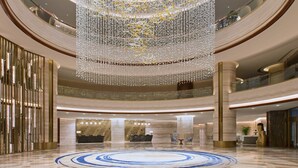 Un'ampia hall con un pavimento circolare grande, a motivi blu e bianchi, un lampadario sontuoso e diversi livelli con ringhiere in vetro.