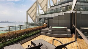 Una terrazza panoramica moderna con vasca idromassaggio e area salotto all'aperto, affacciata su una vista mozzafiato dello skyline cittadino.