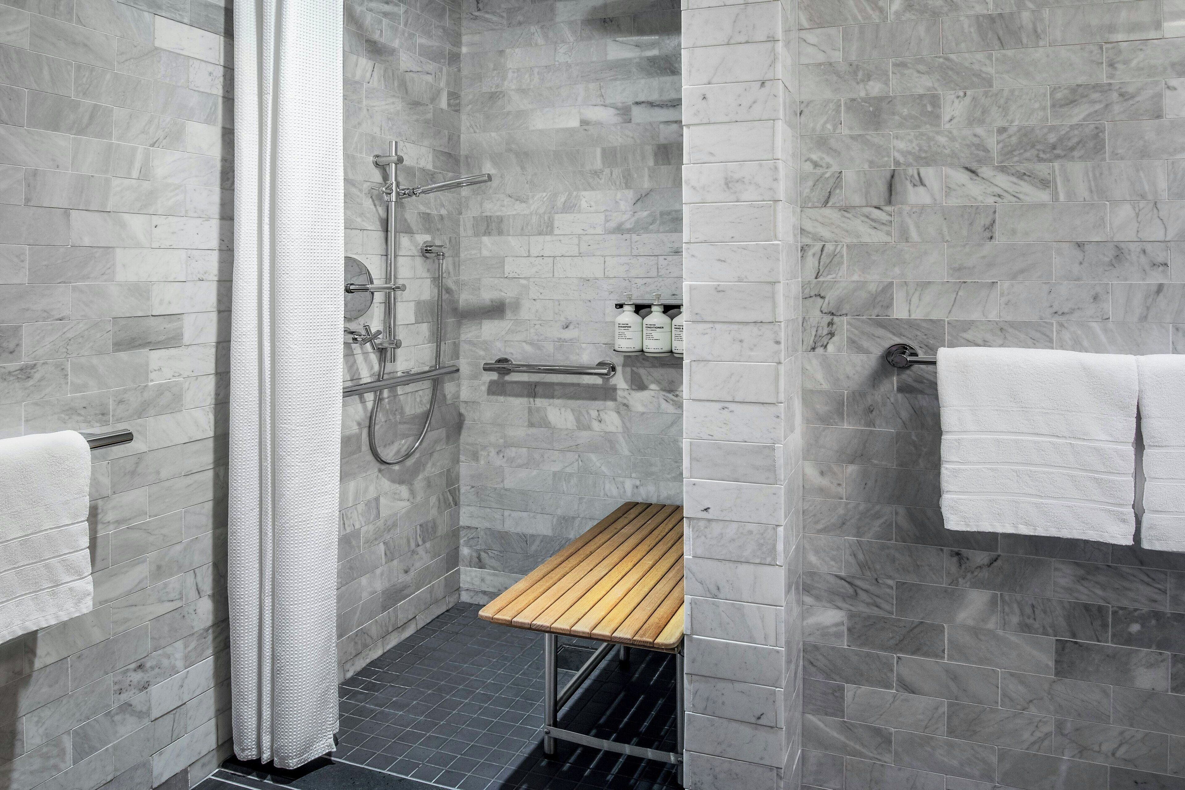 Une salle de bain moderne avec des carreaux de marbre gris, un banc en bois, un porte-serviettes et un espace douche.