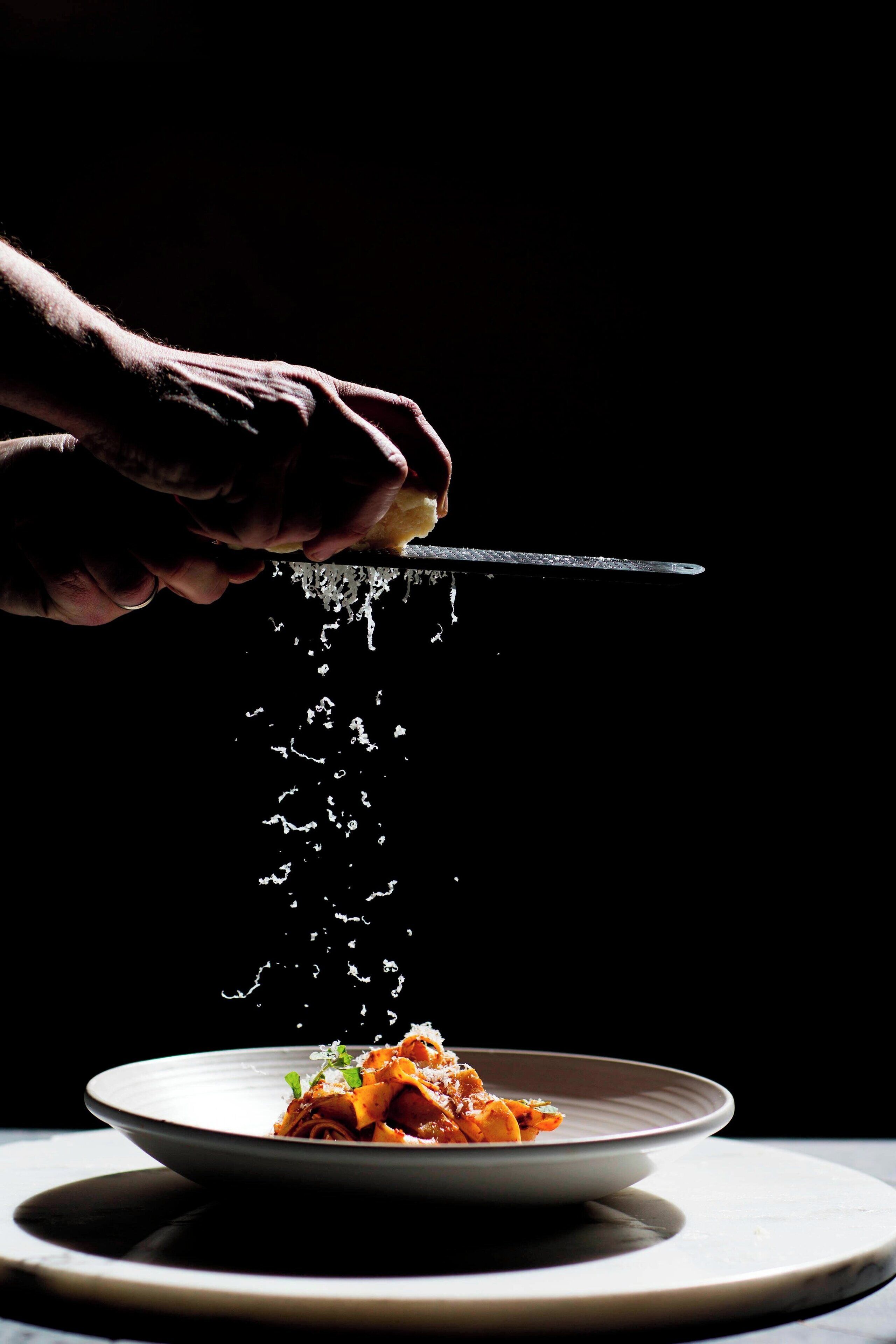 A hand holding a knife above a plate of food, with water droplets visible.