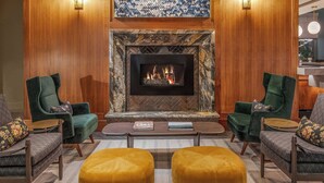 A cozy living room with a fireplace, two green armchairs, a coffee table, and a yellow ottoman. - The Press Hotel, Marriott Autograph Collection (Portland)