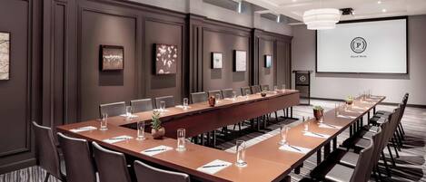 A conference room with a long table, chairs, and a projector screen.