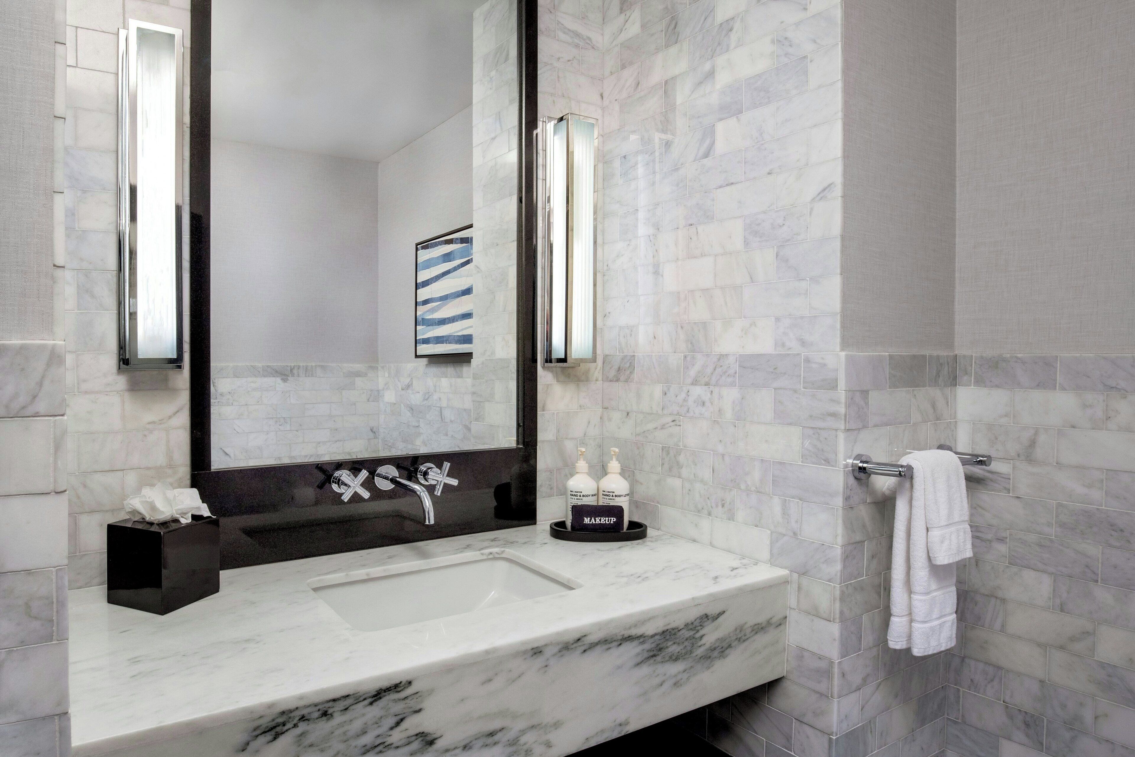 A modern bathroom with a marble sink, a large mirror, and a towel rack.