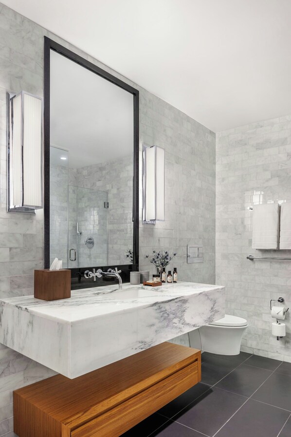 A modern bathroom with a large mirror, marble countertop, wooden vanity, and a toilet with a towel rack.