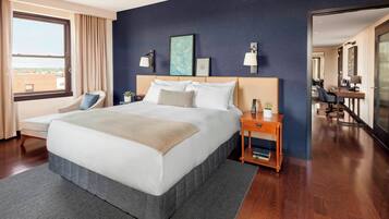 A modern hotel room with a large bed, a desk, a chair, and a view of the city.