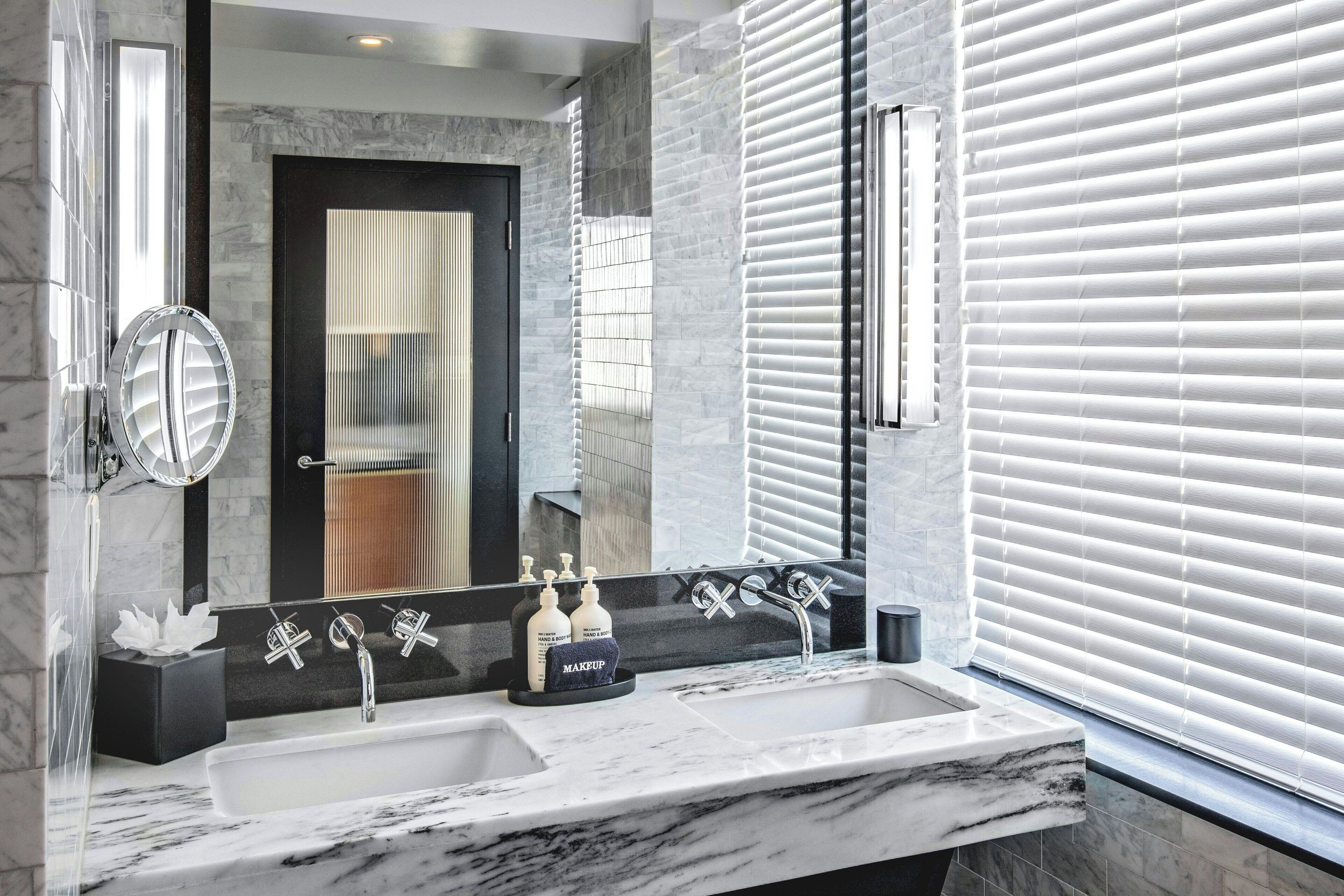 A modern bathroom with a dual sink, large mirror, and a view of the adjacent room.