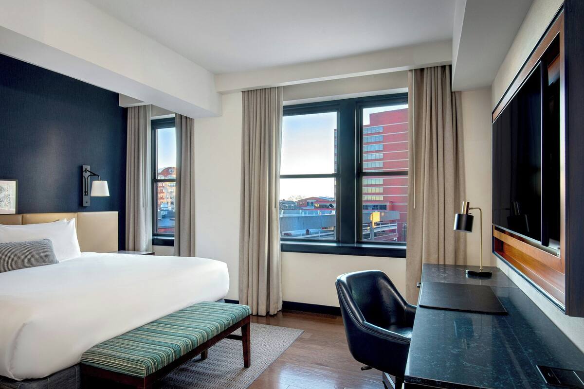 Quarto de hotel com uma cama grande, uma mesa, uma cadeira e uma televisão.