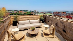 A rooftop terrace with a sofa, two chairs, and a small table, overlooking a cityscape and a body of water. - The Press Hotel, Marriott Autograph Collection (Portland)