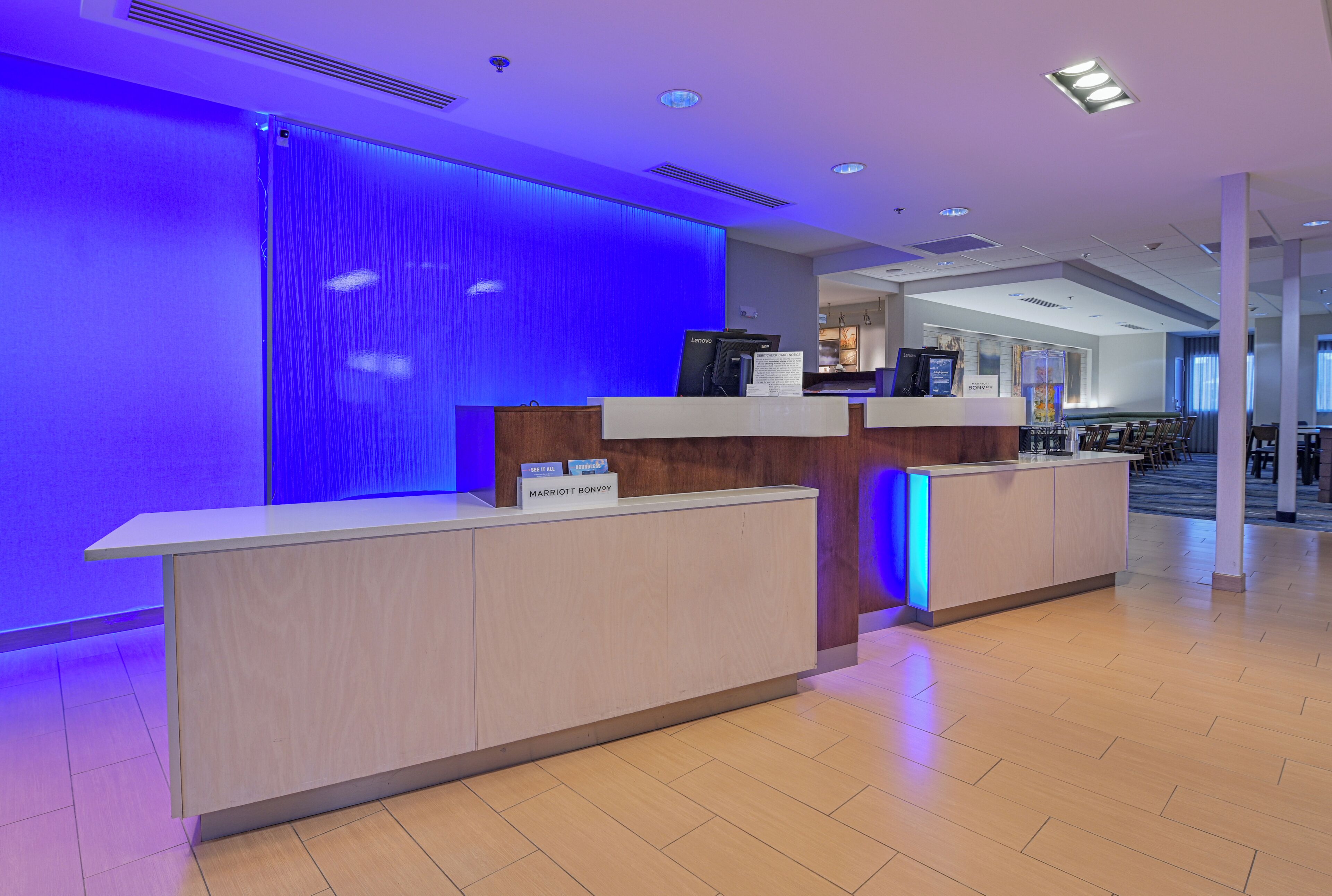 A hotel reception desk with a modern design, a digital screen, and a sign indicating the hotel name.