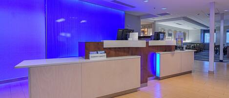 A hotel reception desk with a modern design, a digital screen, and a sign indicating the hotel name.
