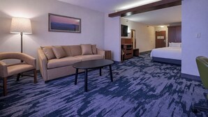 Habitación de hotel con sofá, sillón, mesita y cama.