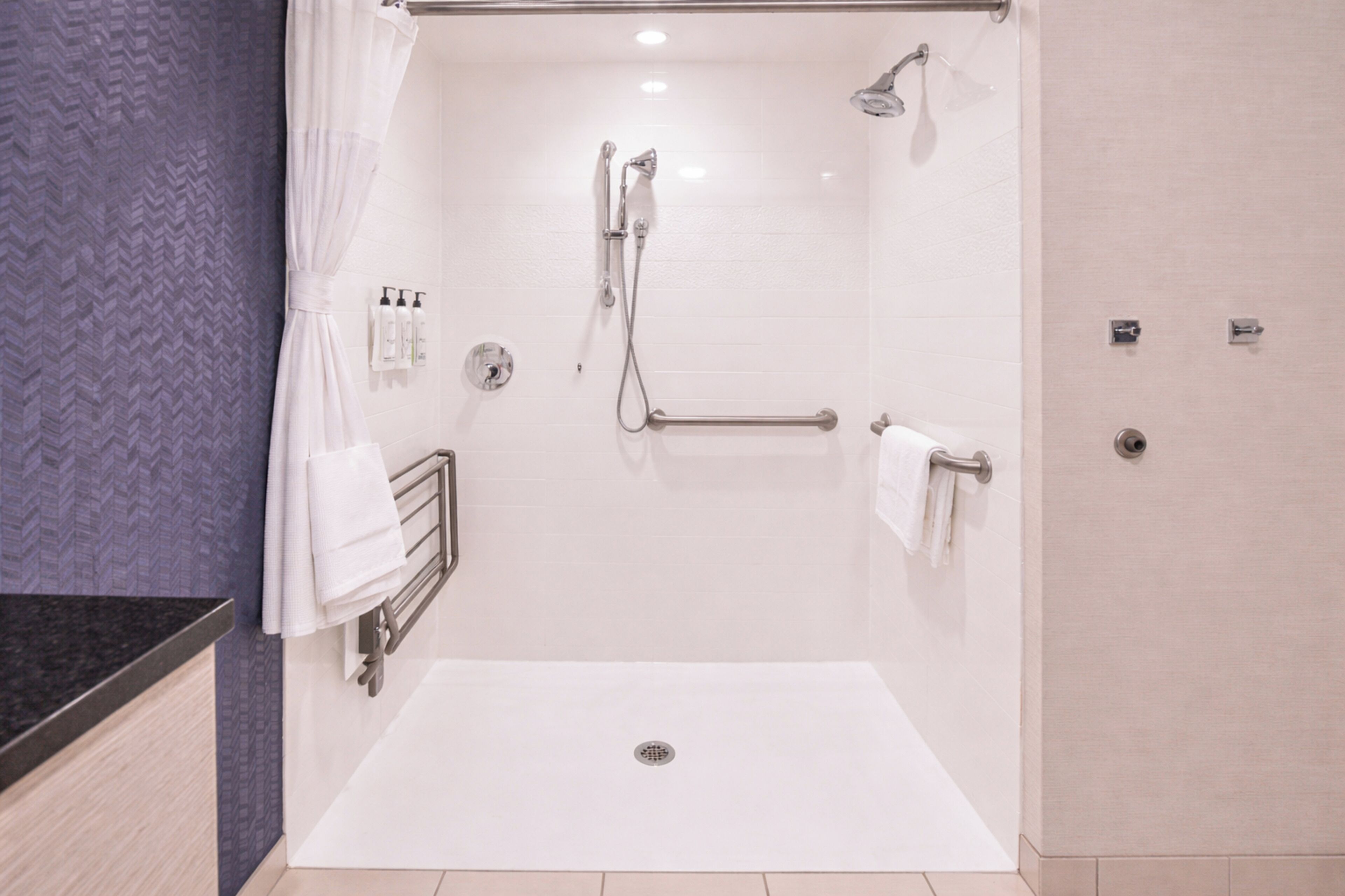 Un baño moderno con cabina de ducha, barras de apoyo y suelo de baldosas blancas.