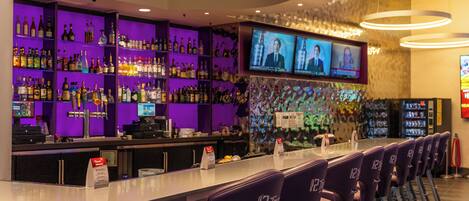 Zona de bar con iluminación morada, varias televisiones y una variedad de botellas de licor.