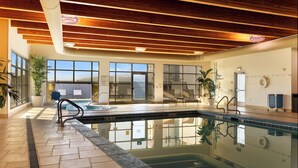 Une piscine intérieure avec des poutres en bois, de grandes fenêtres et des plantes en pot.